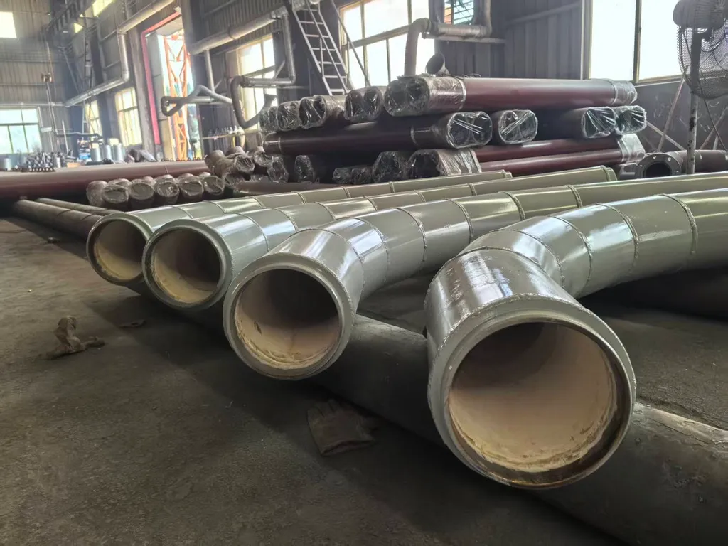 Large-diameter pipes with cream-coloured ceramic-lined ends and grey-green coated exteriors laid out on the workshop floor