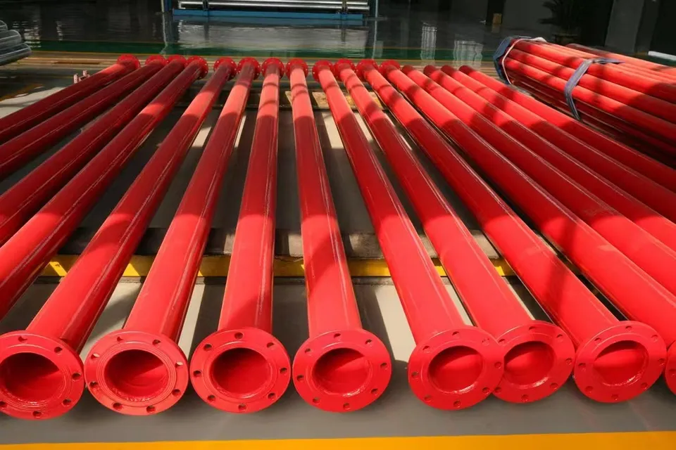 Red painted flanged induction-hardened steel pipes laid out in rows on the workshop floor