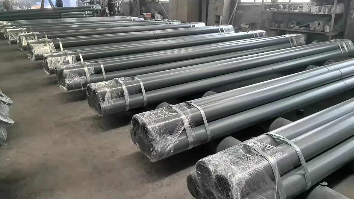 Bundles of long grey SHS ceramic composite pipes stacked in rows on the factory floor, strapped with metal bands and with the ends wrapped in clear film