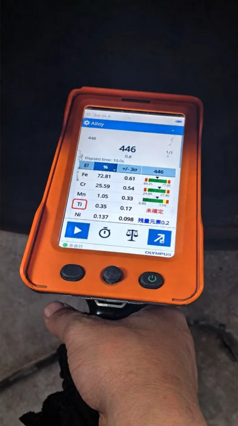 Handheld XRF alloy analyzer in its protective sleeve, with the alloy reading on its screen