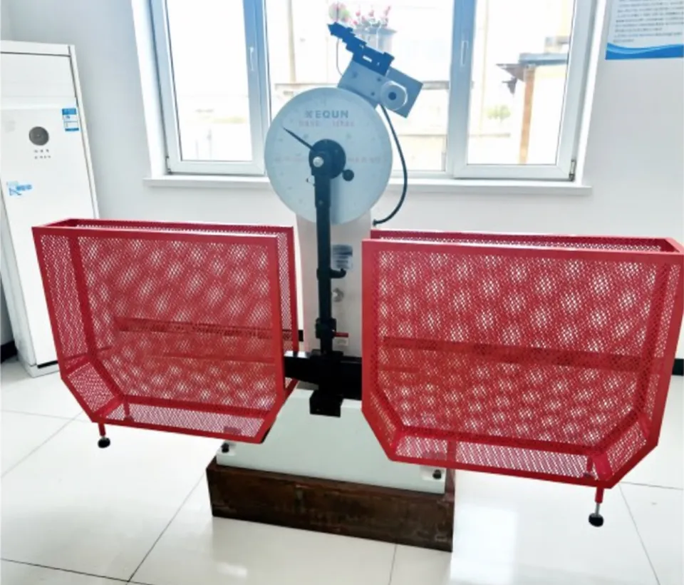Pendulum impact testing machine with its dial, pendulum arm and red mesh safety guards