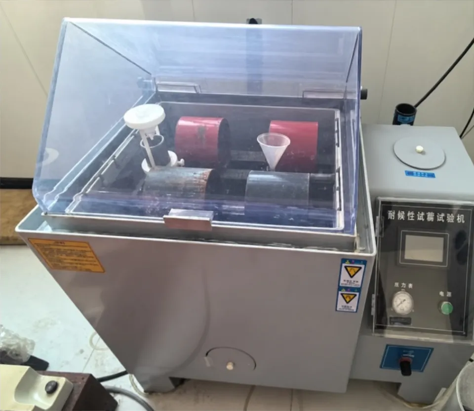 Salt spray test chamber with a transparent lid over the test chamber and a control cabinet beside it